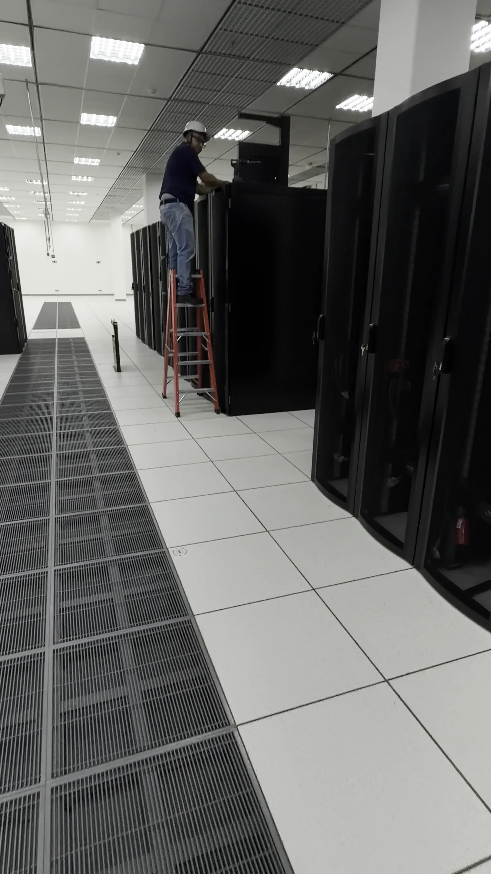 A technician working at a server cabinet inside a data-center aisle.